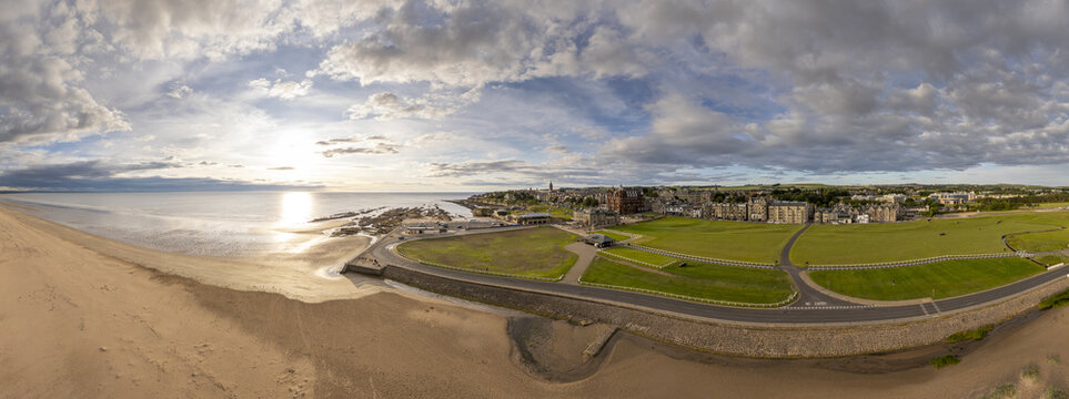Aerial view of the golden beach meeting the calm sea, adjacent to the lush green fields and historic buildings of St Andrews, Scotland, United Kingdom.