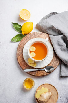 Cup of ginger lemon tea with honey and fresh ingredients on a light background.