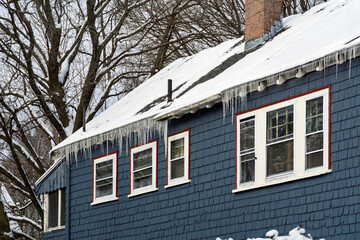 Beautiful but potentially dangerous large icicles hanging from the eaves of a snow-covered roof in Boston, Massachusetts, USA
