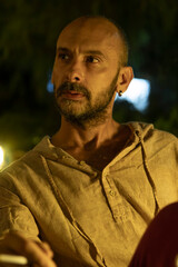A portrait of a mature man sitting at a cozy outdoor cafe table during a warm summer evening, enjoying a cup of coffee. He looks relaxed and thoughtful in a modern urban lifestyle setting.