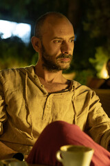 A portrait of a mature man sitting at a cozy outdoor cafe table during a warm summer evening, enjoying a cup of coffee. He looks relaxed and thoughtful in a modern urban lifestyle setting.