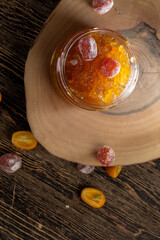 orange jam with dried kumquat fruits in sweet sugar syrup, sweet jam for making desserts in a round glass jar on a wooden table, orange jam made from oranges and fresh citrus fruits
