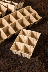 empty cardboard pots for seedlings scattered in a field with fertile soil, soil mixed with humus and peat, and paper disposable cups for seedlings in spring