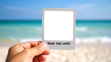 Hand holds an instant photo frame with 'Save the date' text over a tropical beach. Concept for wedding or event announcement with a transparent background for easy overlay and composition.
