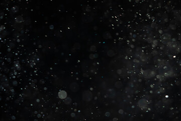 Obraz premium Soaring little pieces of dust floating in a ray of light on a black background. Twirling randomly as if blown by wind moving quickly through space. Each of them flying independently and dynamically.