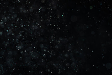 Soaring little pieces of dust floating in a ray of light on a black background. Twirling randomly as if blown by wind moving quickly through space. Each of them flying independently and dynamically.