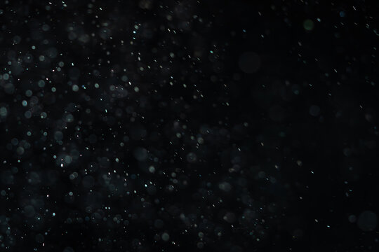 Soaring little pieces of dust floating in a ray of light on a black background. Twirling randomly as if blown by wind moving quickly through space. Each of them flying independently and dynamically.