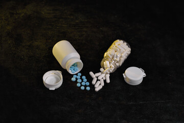Close-up view of various white capsule pills and small blue tablets scattered from two overturned medicine containers, symbolizing medication management, healthcare and pharmaceutical concepts.