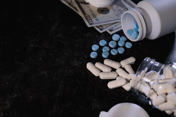 Scattered pharmaceutical pills, both white capsules and blue tablets, emerge from overturned plastic bottles, contrasting with US currency suggesting pharmaceutical cost or illicit transactions