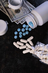 Pharmaceutical capsules and tablets in blue and white colors spill from open containers beside US currency. High cost of medicine, medication expenses, or pharmaceutical trade concepts effectively.
