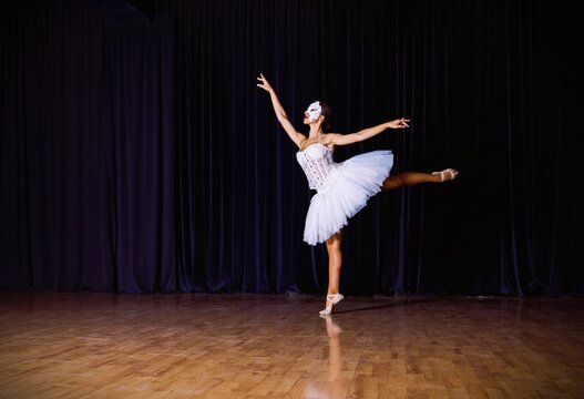 Dance performer practices ballet routine on stage during a rehearsal in a dark theater
