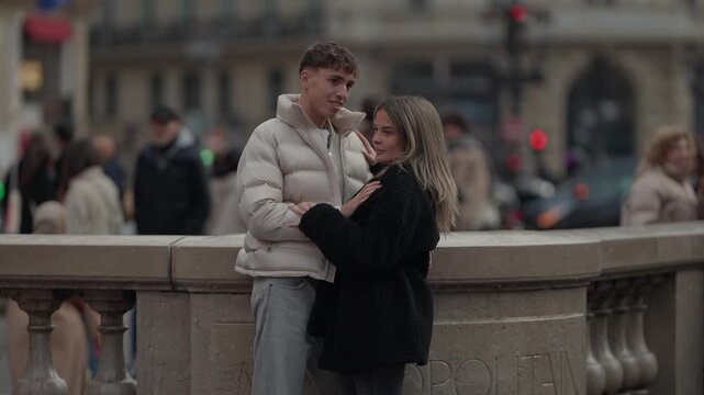A young couple shares a romantic moment in Paris France The man and woman are embracing outdoors in an urban setting with a blurred background of city streets and buildings The scene captures a tender