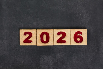 New Year 2026. Holiday Square cookies with red marmalade filling in the shape of the numbers 2026. Dark background. Top view