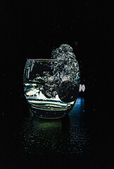 Fresh orange cherry tomato falling into a glass of water with a big splash, high speed photography on a black background.