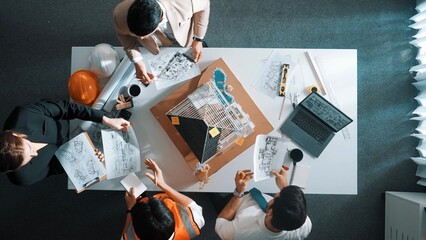 Top view of manager handed blueprint to professional engineer team at meeting table with house model and project plan. Group of architect discussing about design while receive document. Alimentation.