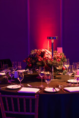 A beautifully set round banquet table decorated with Christmas floral centerpiece, candles, and glassware under purple ambient lighting.

