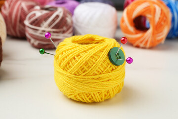 Ball of yellow yarn with pins and button on white table, closeup