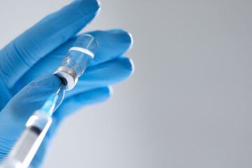Nurse taking vaccine from vial with syringe on light background, closeup. Space for text