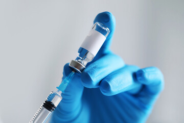 Nurse taking vaccine from vial with syringe on light background, closeup. Space for text