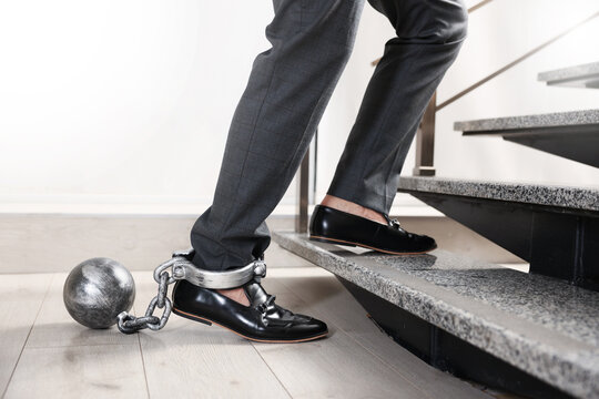 Businessman walking up stairs with metal ball and chain on his leg indoors, closeup