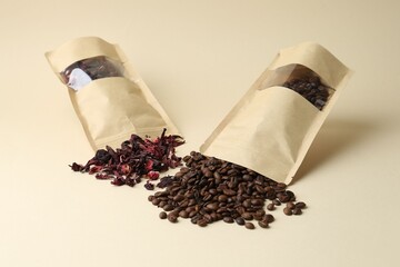Stand-up pouches with coffee beans and flower tea on beige background, closeup