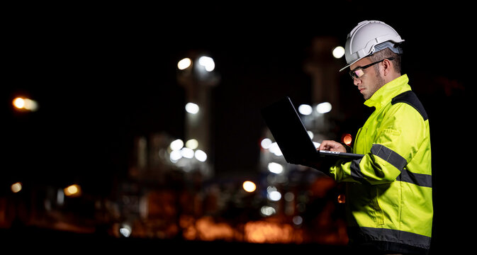Industrial engineer night inspection at refinery or petrochemical plant walkie-talkie hand and digital tablet intersection of technology, worker work at night at power plant