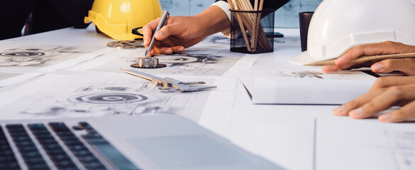 Engineers collaborate on detailed blueprints in a modern office, showcasing design tools, construction helmets, and a laptop on the table for an efficient workflow. SACTR