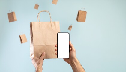 Hands hold a smartphone and brown paper bag, conceptually showing online shopping delivery on a light blue studio background.
