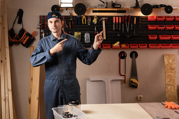 young carpenter pointing with fingers on advertisement space while assemble furniture working in studio or workshop with tools on walls. woodworking workshop
