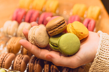 Woman holding French macarons in her hand against a yellow background, bright and modern composition, sweet gourmet dessert, lifestyle food photography 