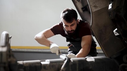 Professional mechanic performing diagnostics and servicing a vehicle engine, using a wrench to tighten bolts in an auto repair workshop