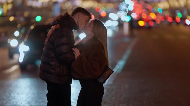 A young couple embraces on a street in Paris France at night The city lights are blurred in the background creating a romantic atmosphere The lovers share an intimate moment on a city street.