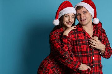 Fototapeta premium Happy couple in Santa hats and pajamas on light blue background. Christmas atmosphere