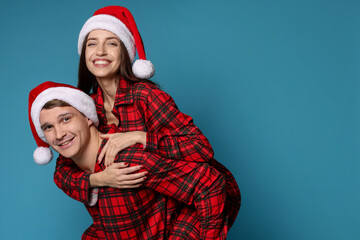 Fototapeta premium Happy couple in Santa hats and pajamas on light blue background. Christmas atmosphere