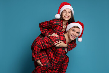Fototapeta premium Happy couple in Santa hats and pajamas on light blue background. Christmas atmosphere