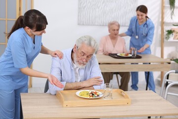 Care worker serving dinner and comforting senior man at retirement home