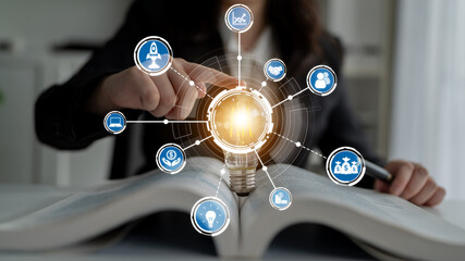 A person points at a light bulb on an open book, with digital icons symbolizing innovative business ideas, strategies, and growth opportunities. Perfect for business themes. Crux