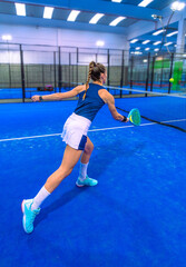 Rear view of an athletic woman playing padel in perfect hand and foot position, hitting the ball with a backhand near the net.