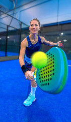 Action shot of a padel ball flying towards the camera after being hit by a backhand shot from a female padel player in perfect position, smiling happily at her technique.