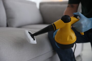 Pest control worker cleaning sofa with steam cleaner indoors, closeup