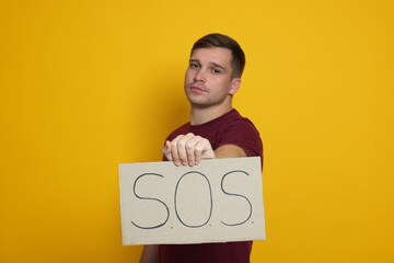 Man holding sign with word SOS on yellow background