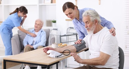 Caregiver measuring senior man's blood pressure at home