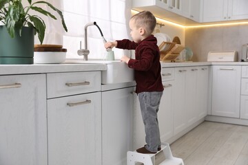 Child safety at home. Little boy pulling down faucet hose in kitchen