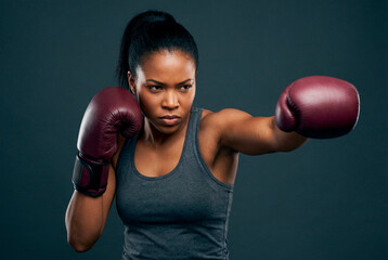 Focused african american woman boxer training with punching stance and maroon gloves against dark background