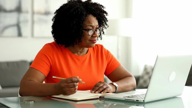 Smiling Mature Black Woman Working on Laptop and Taking Notes at Home