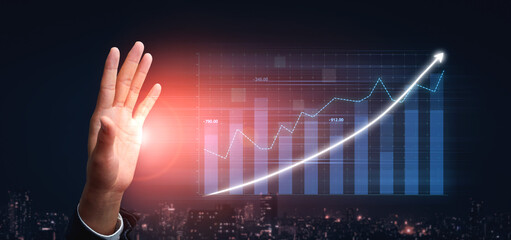 A businessman uses his hand to signal growth, with a digital graph overlay showcasing positive trends against a night urban skyline, illustrating progress. Impute