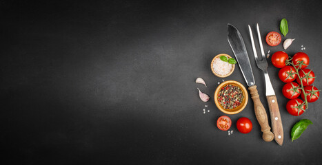 Cooking background with fresh cherry tomatoes, spices, cutlery and herbs on black slate surface...