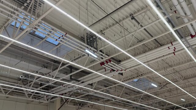Industrial Warehouse Ceiling With Skylight Panels Showcasing Grid Of LED Fixtures, Metal Rafters, Ventilation Ducts, And Maintenance Access Points Creating Bright Daylight Interior