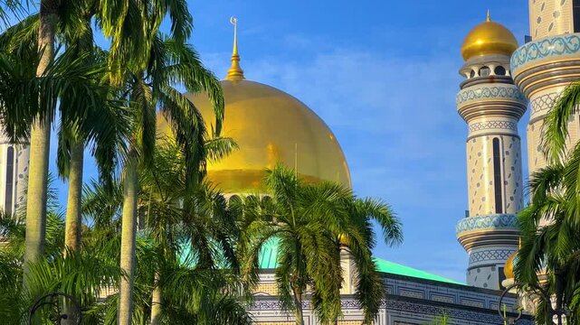 The golden dome and building of the Jamil Asra Hassan Al-Bolkiah Mosque in Bandar Seri Bagawan, Brunei Darussalam, are framed by tropical palm trees on a sunny day. Asia. 4К