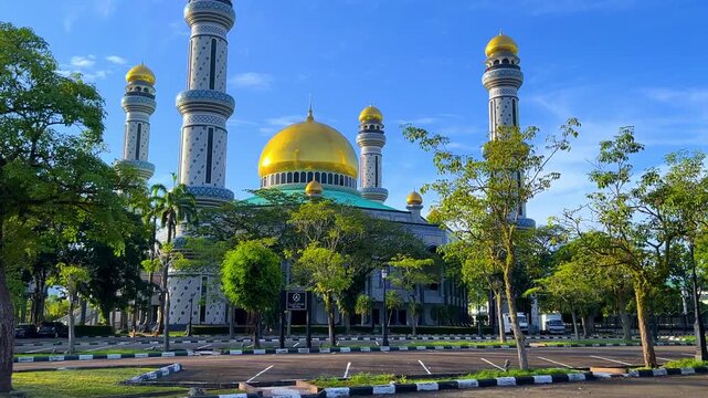 The golden dome and building of the Jamil Asra Hassan Al-Bolkiah Mosque in Bandar Seri Bagawan, Brunei Darussalam, are framed by tropical palm trees on a sunny day. Asia. 4К